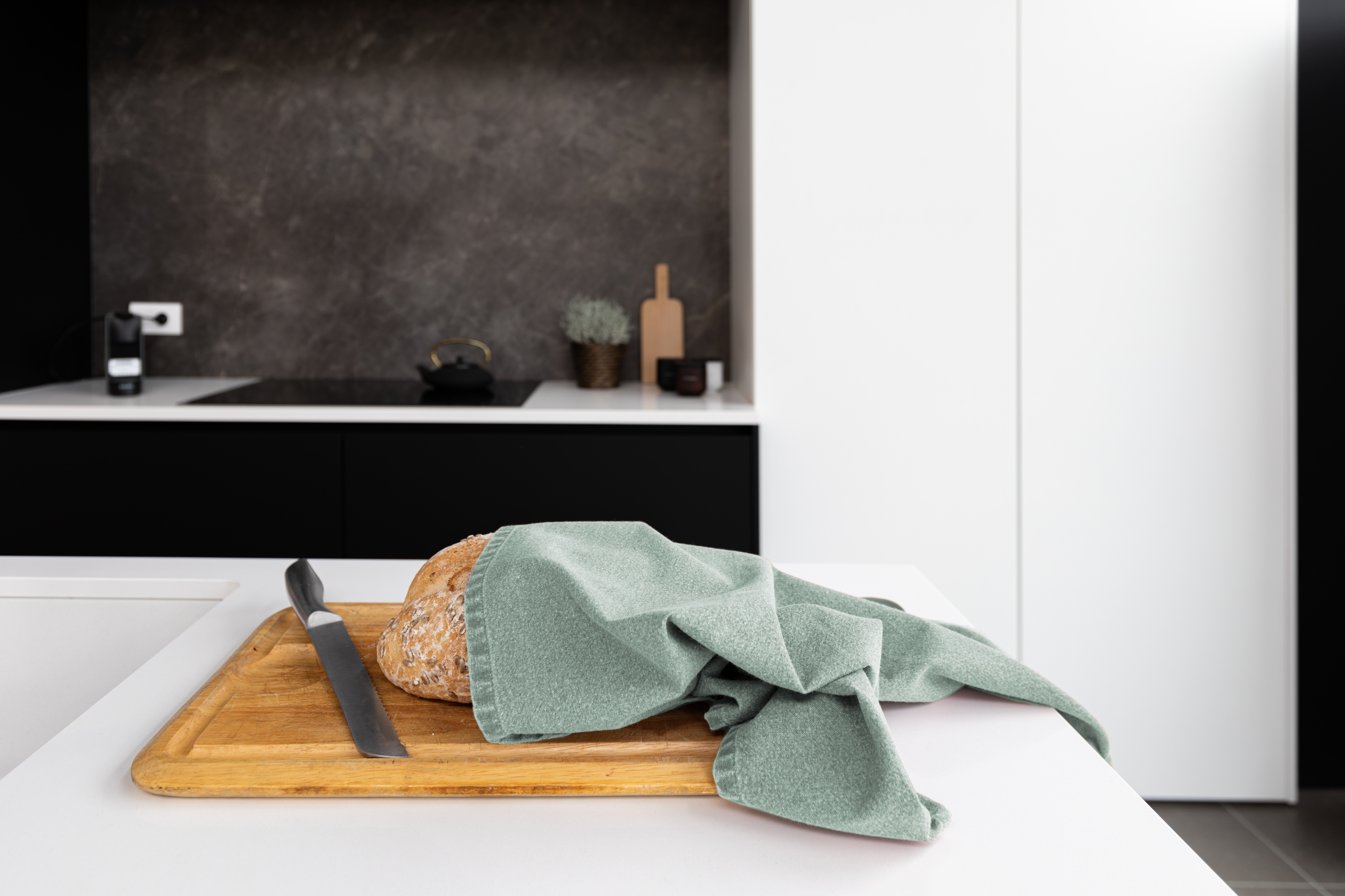 A kitchen towel is wrapped around a loaf of bread that is placed on a cutting board.