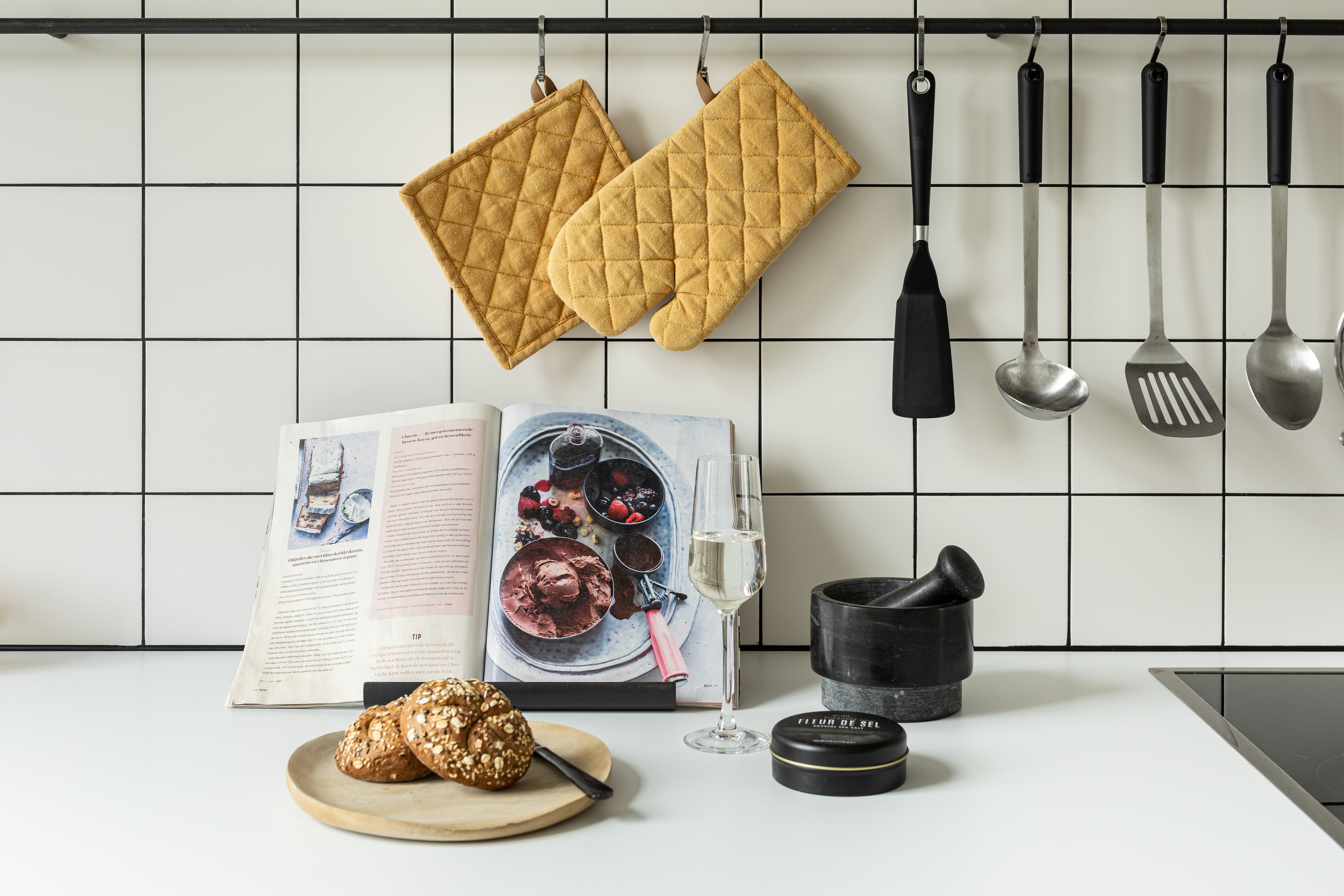 Een gele pannenlap en ovenwant hangen aan de muur van een keuken.