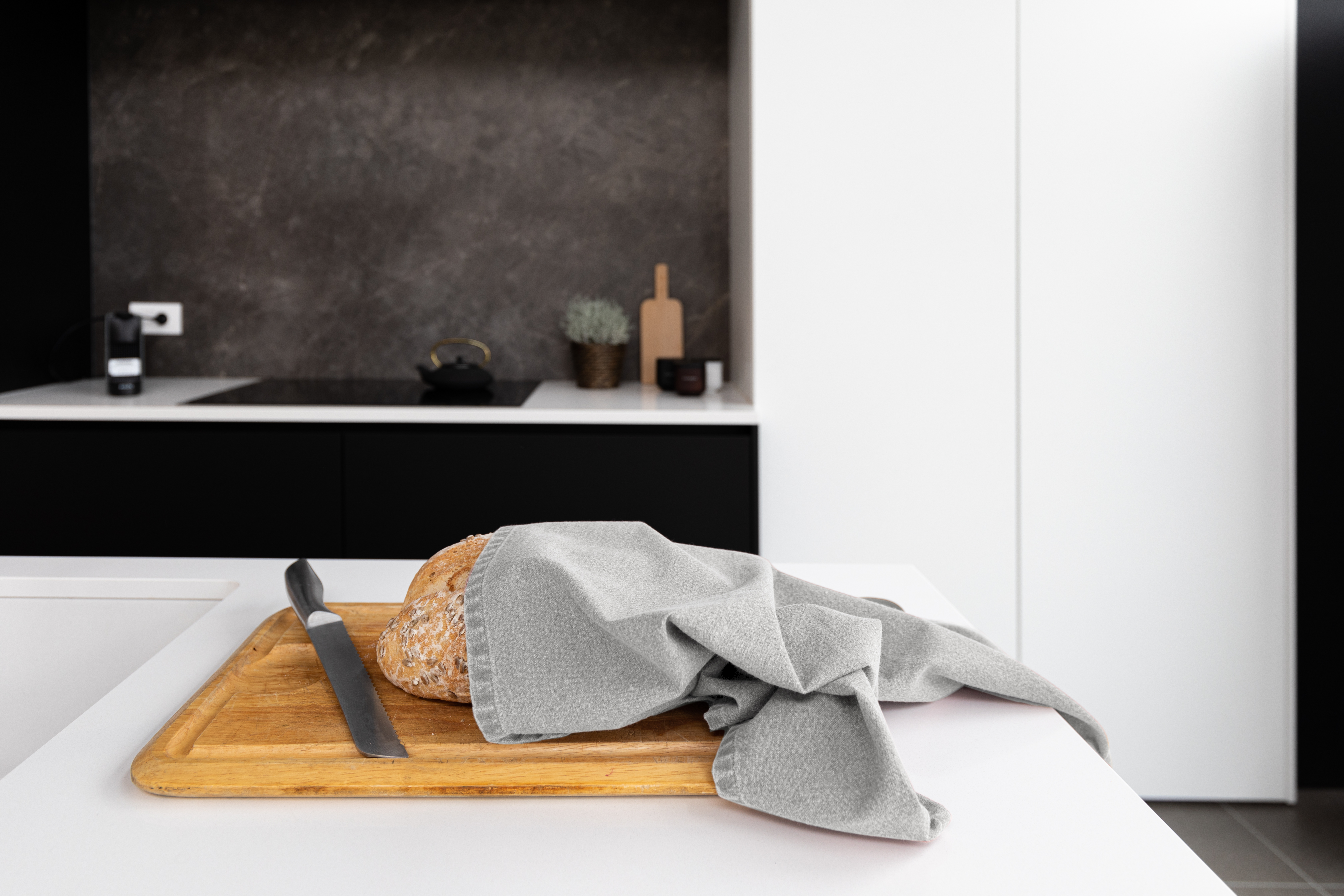 A kitchen towel is wrapped around a loaf of bread that is placed on a cutting board.