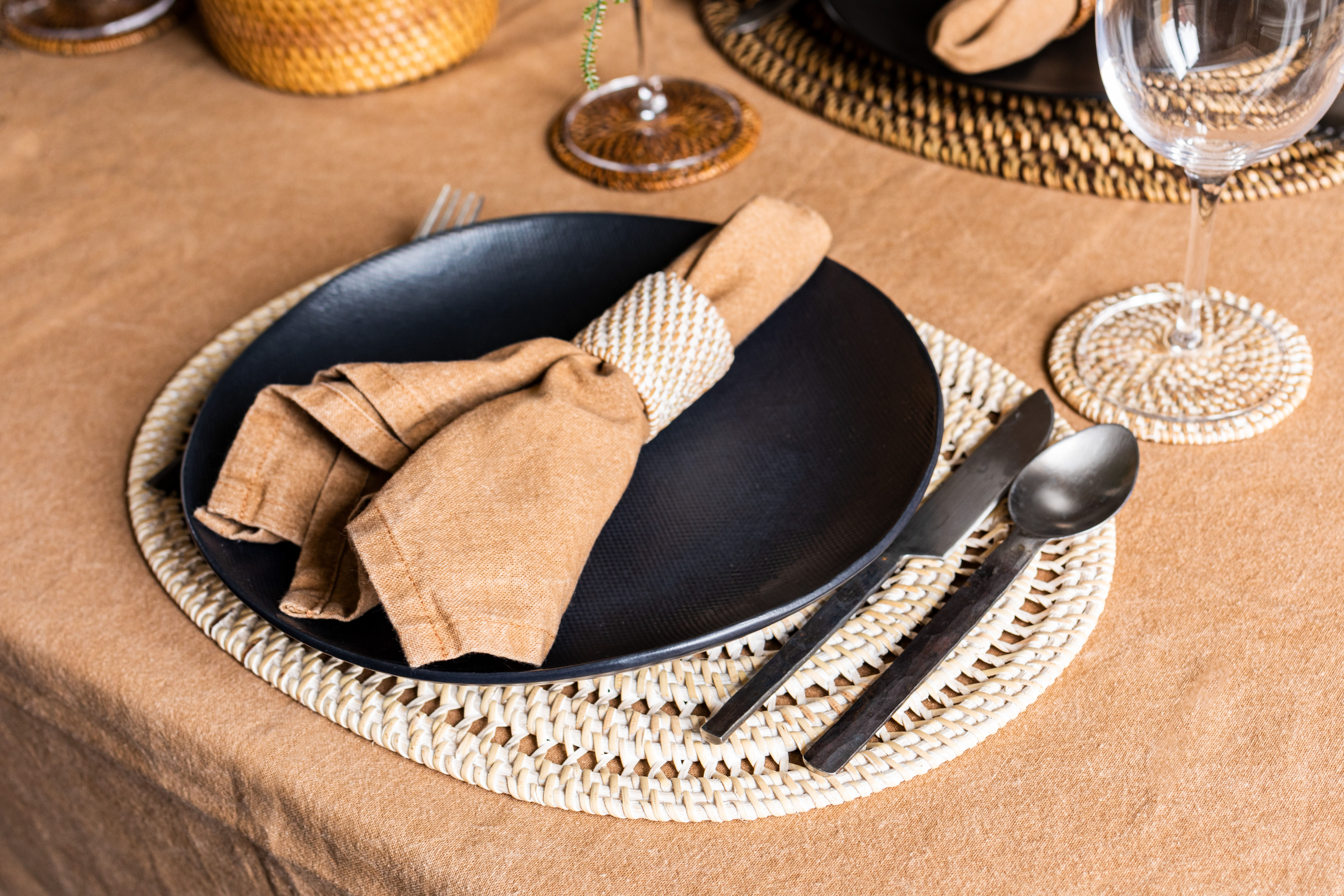 Table decoration with a white oval placemat, napkin rings, glass coasters in rattan material. Napkin and tablecloth in indiantan.
