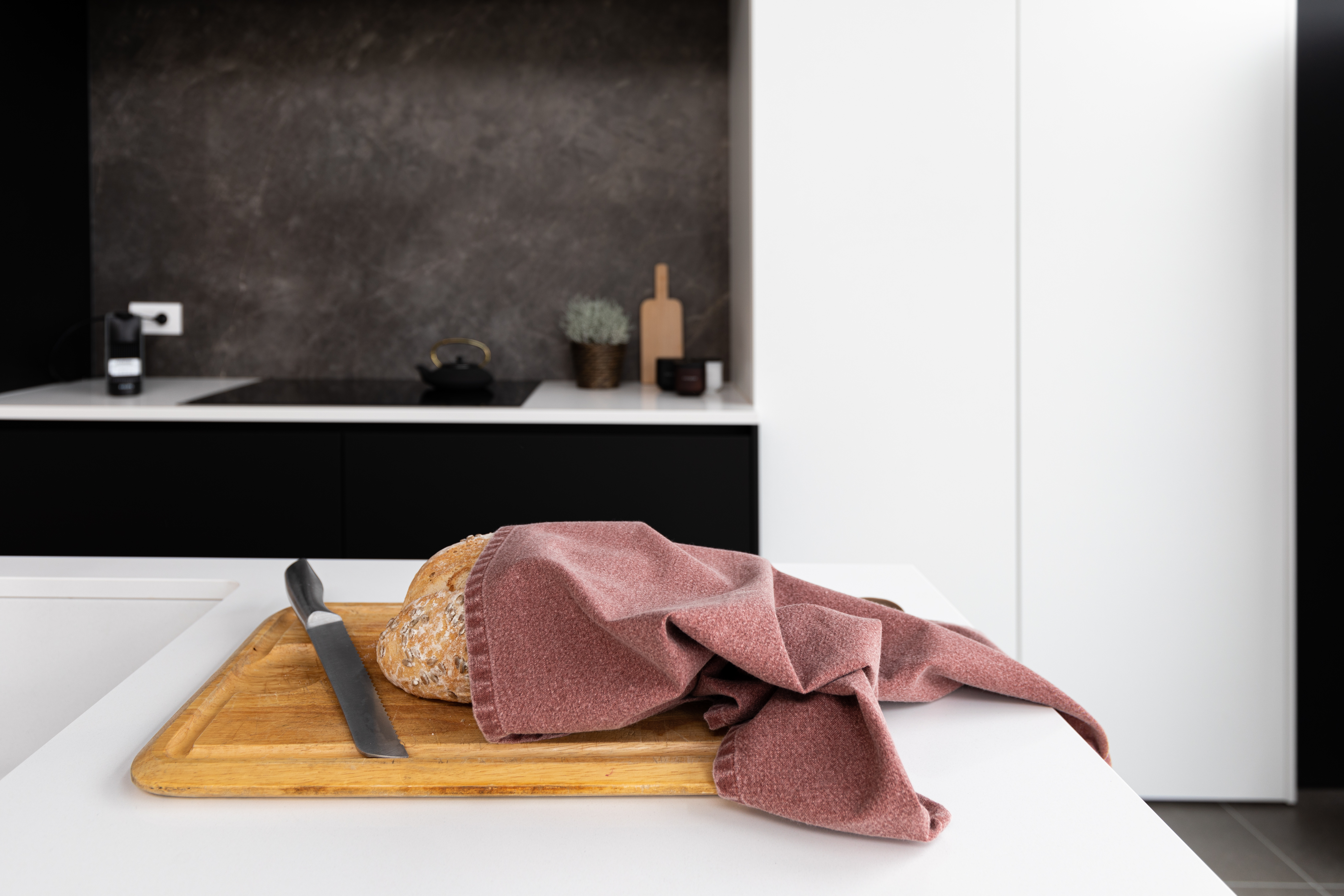 A kitchen towel is wrapped around a loaf of bread that is placed on a cutting board.