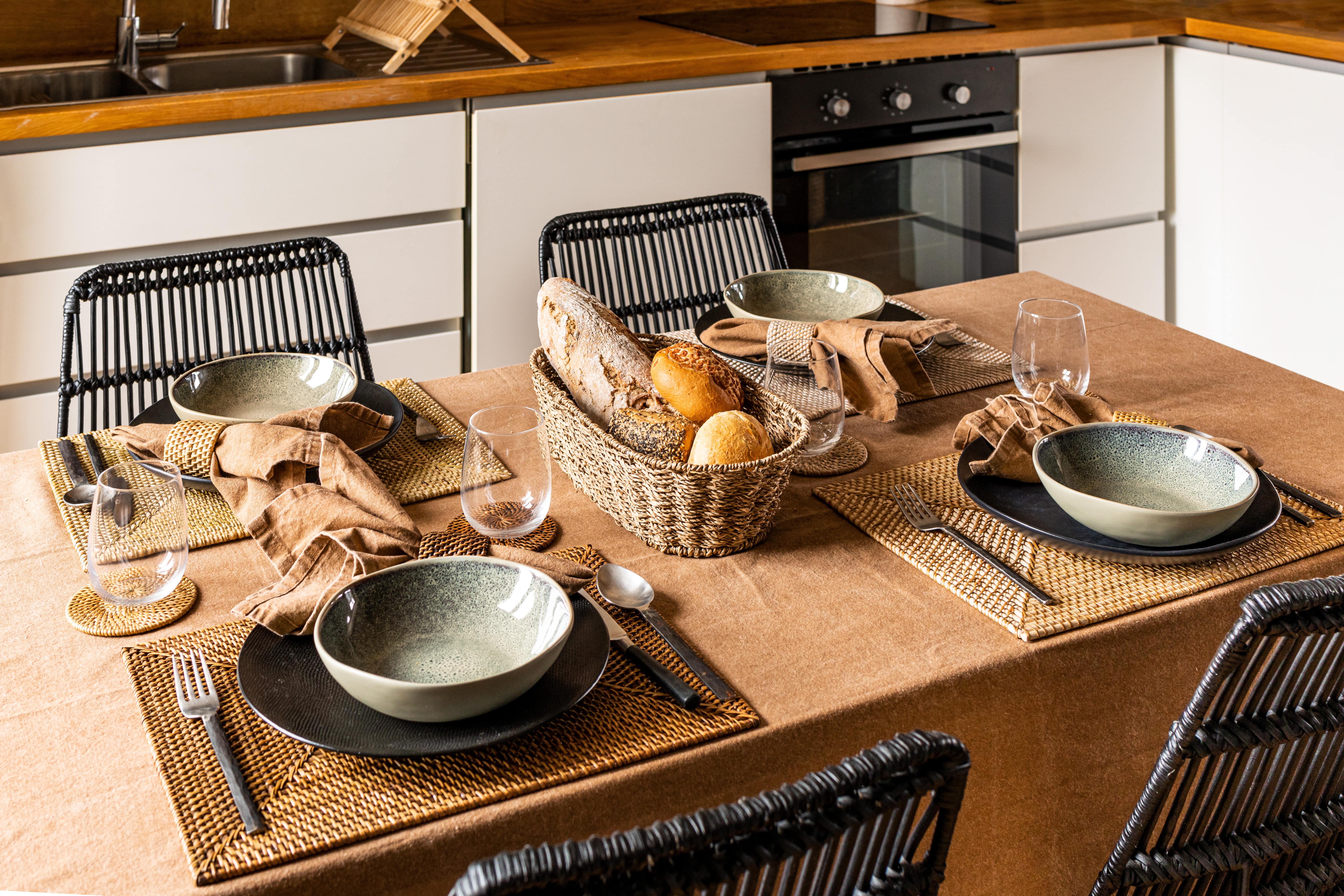 Een gedekte tafel met rechthoekige placemats, glasonderzetters en servet met servetring in Rattan materiaal