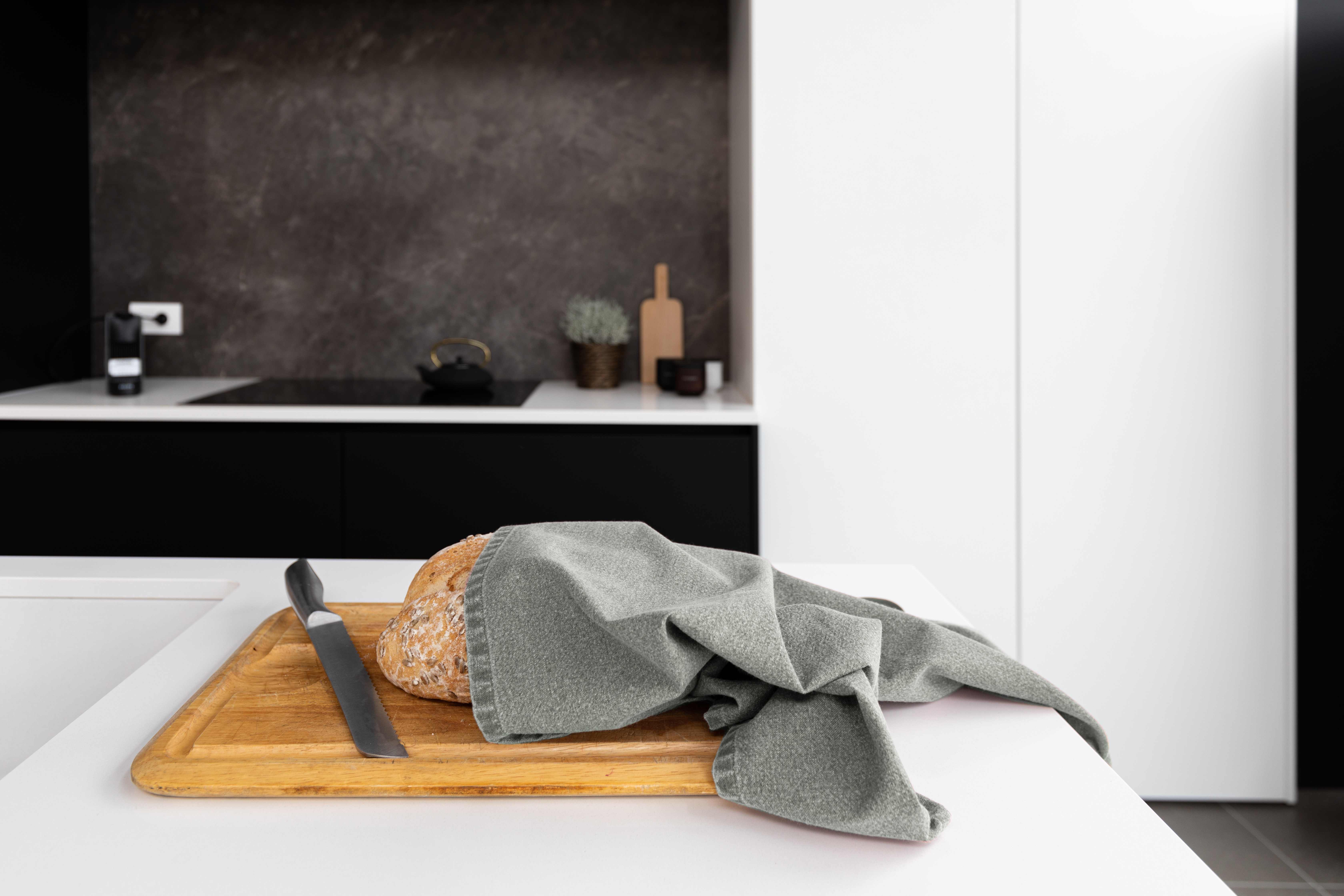 A kitchen towel is wrapped around a loaf of bread that is placed on a cutting board.