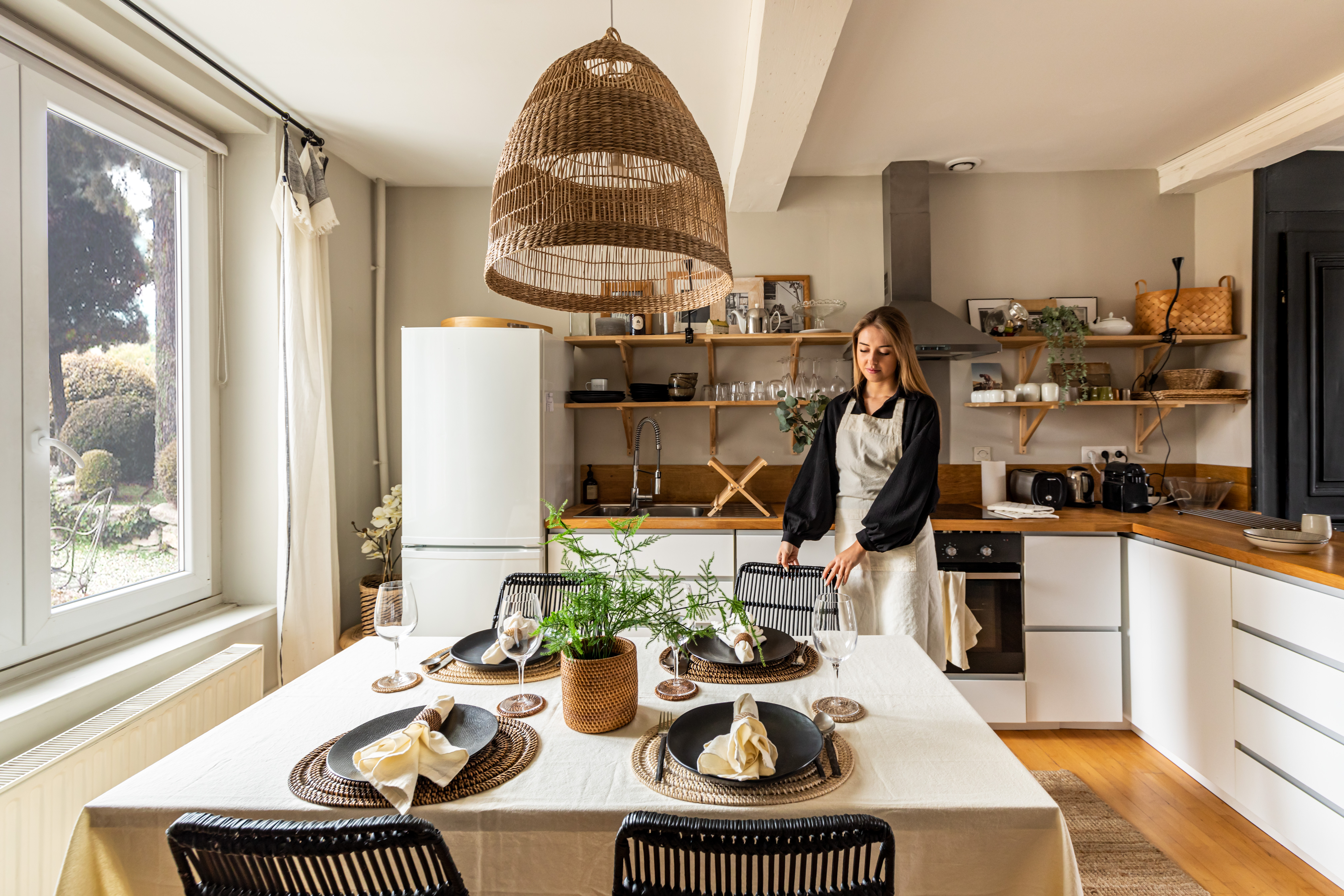 Girl in kitchen apron. A set table with matching tablecloth and napkin. Round placemat, napkin, napkin ring in rattan.